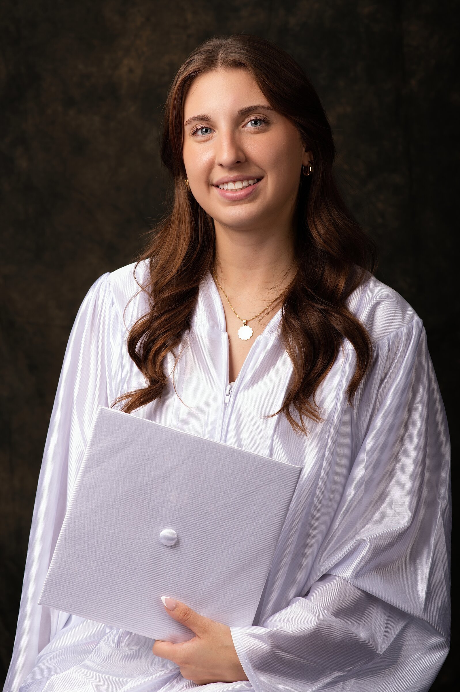 Senior portrait in a white graduation gown holding a diploma folder