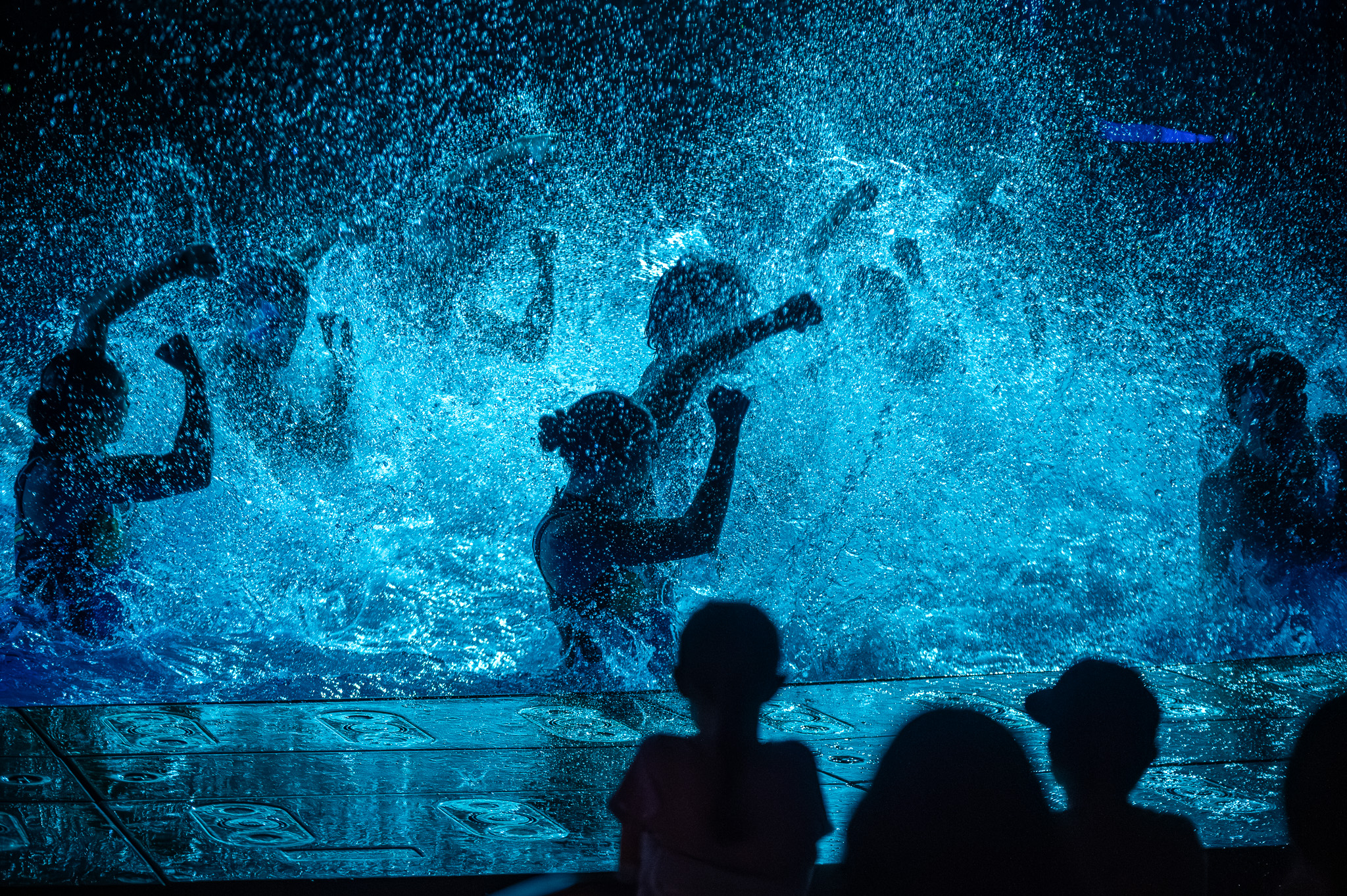 Performer hitting a split through water jets and stage light