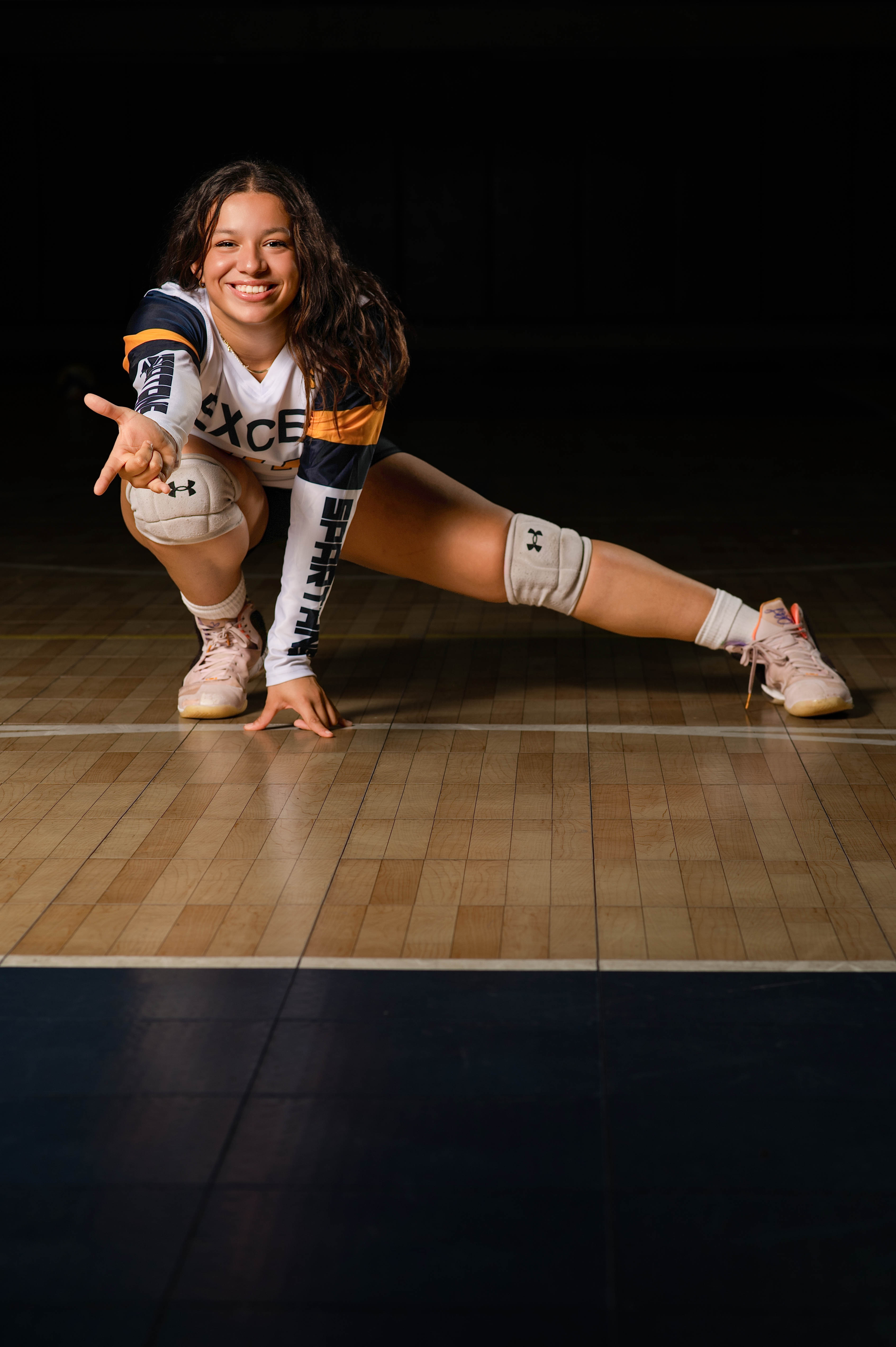 Volleyball senior portrait crouched on the court with a playful point