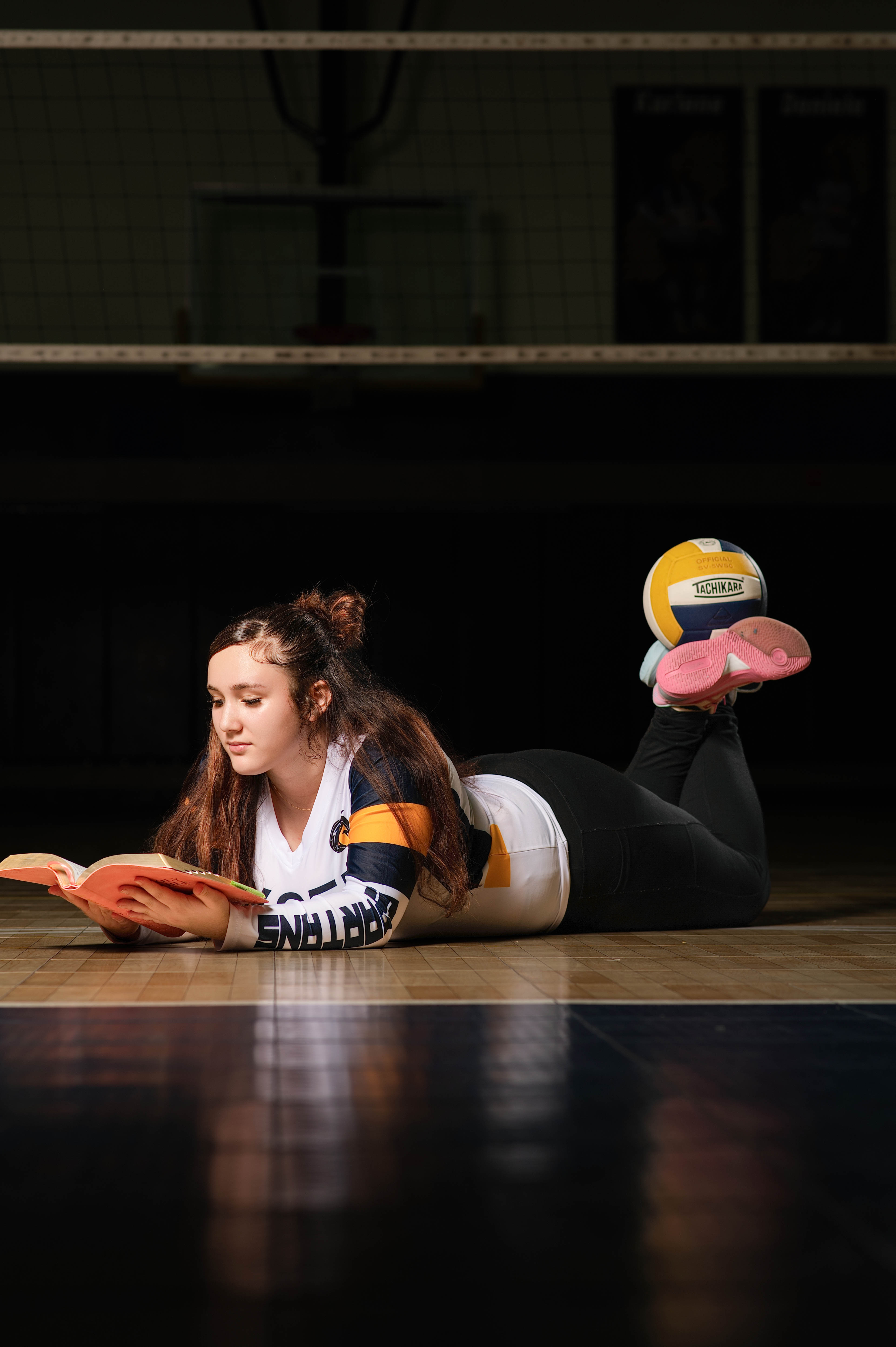 Volleyball senior portrait lying on the court reading a book